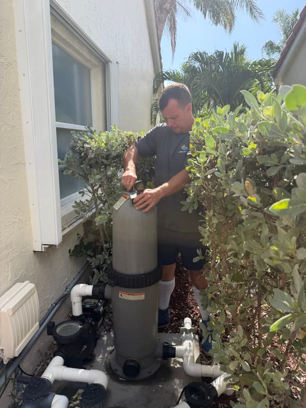 Pool technician opening a cartridge filter housing to inspect the filter element during a weekly service visit