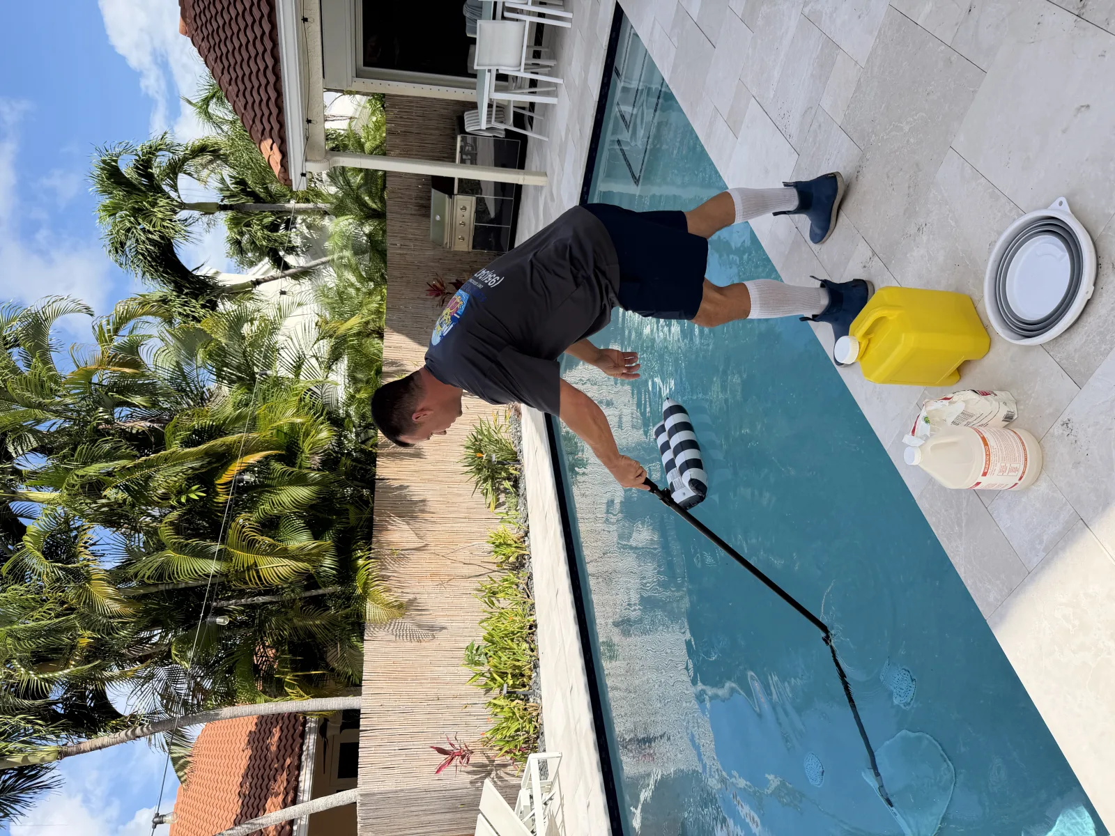 Florida's Best Pools technician brushing the walls of a Delray Beach residential pool on a route visit — the 8–12 minute step that gets skipped on low-bid quotes