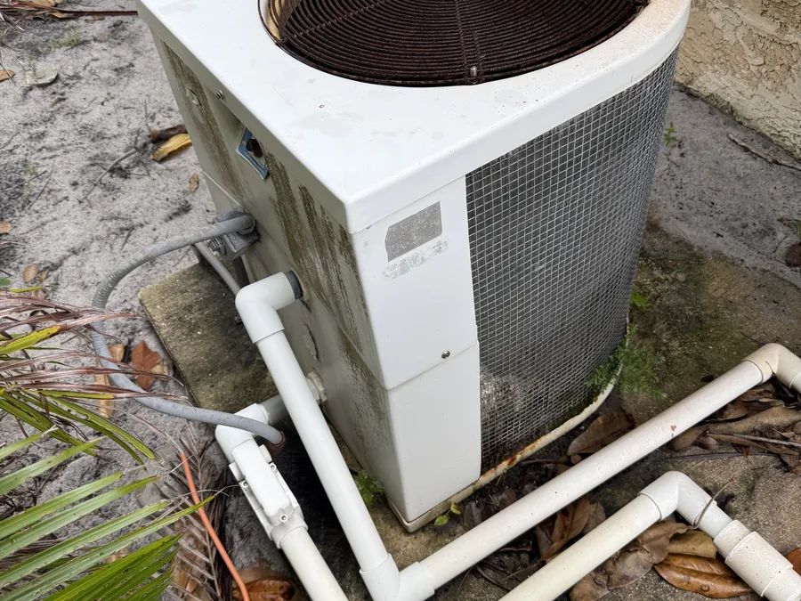 An old, weathered pool heater past its service life on a South Florida equipment pad — faded cabinet and corroded fittings signaling it's time to replace rather than repair